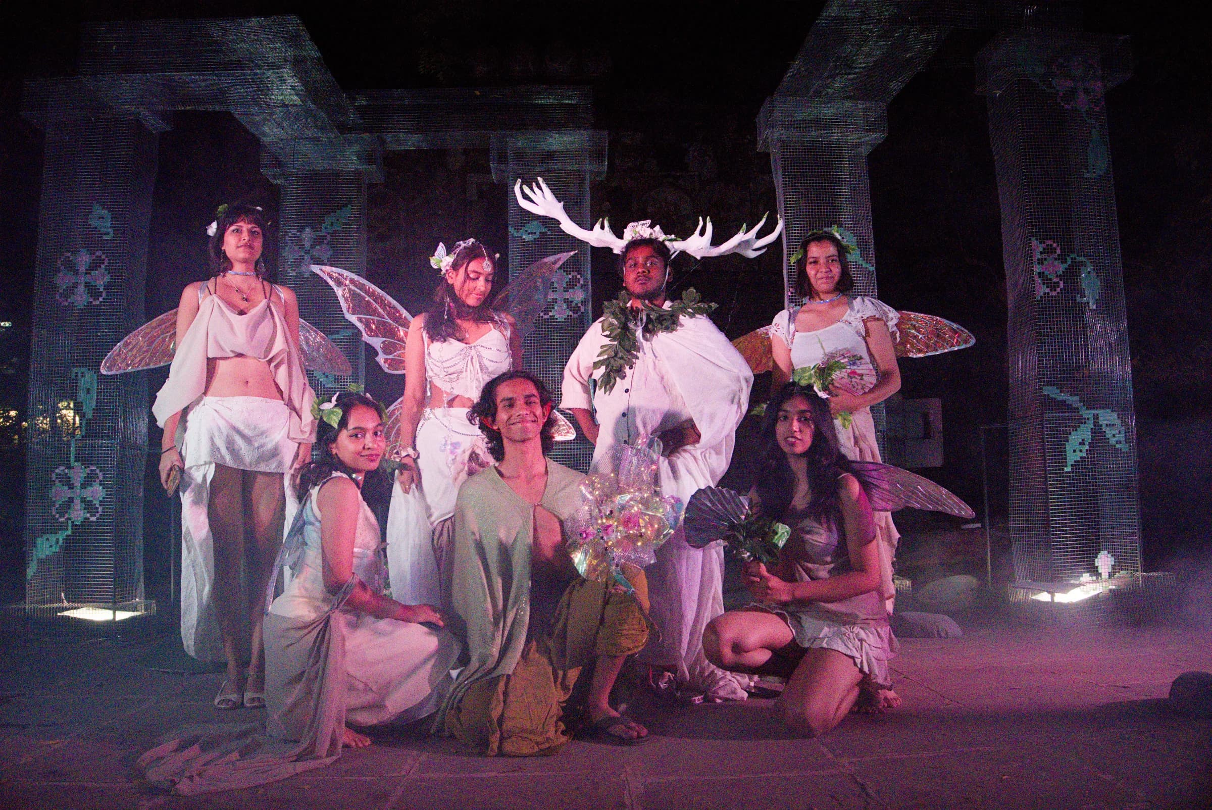 Ensemble in winged and botanical costumes among illuminated stage columns