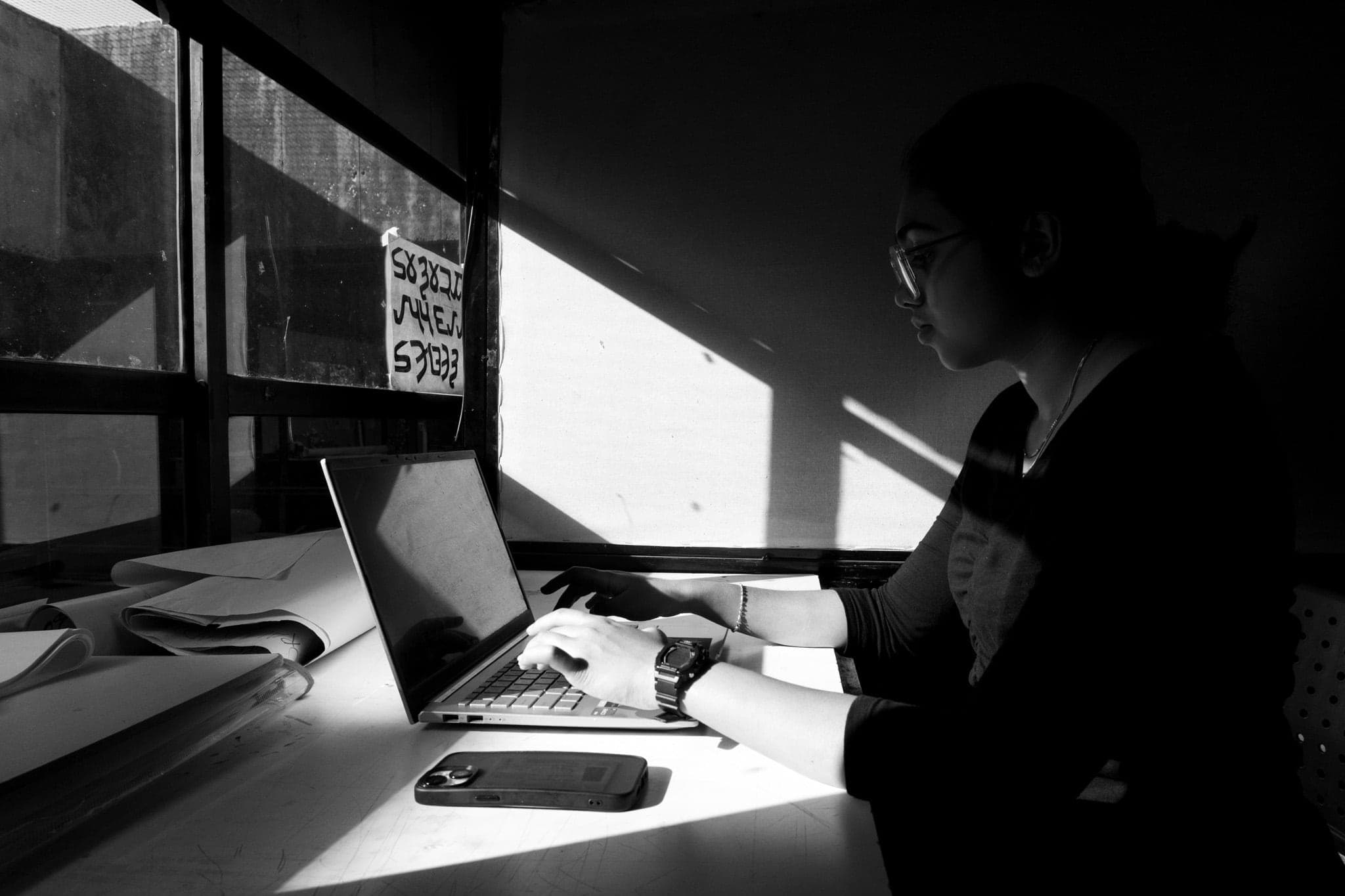 A figure working beside a sunlit window